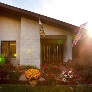 A cozy house with two flags displayed, surrounded by a colorful garden under the warm sunlight.