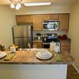 A modern kitchen featuring wooden cabinets, stainless steel appliances, and a small dining area.