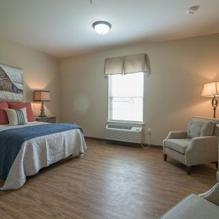 A cozy bedroom featuring a bed, armchair, and soft lighting.