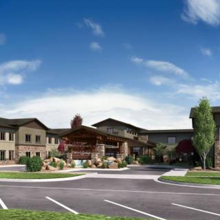 A modern residential building with a landscaped entrance and parking lot under a clear blue sky.