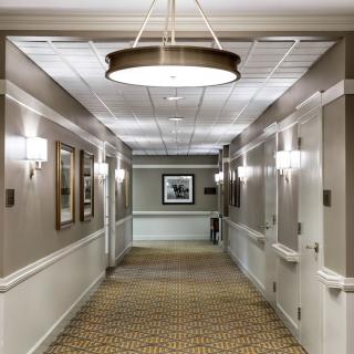 A well-lit hotel hallway with framed artwork and patterned carpet.