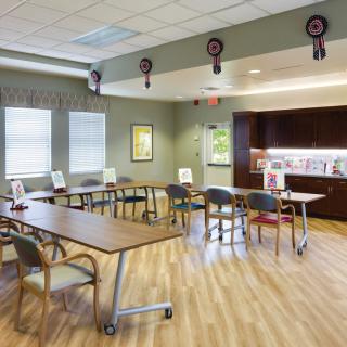 A well-lit classroom with multiple tables and chairs, featuring a wooden floor and wall decorations.