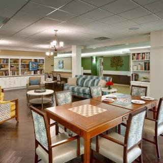 A cozy and well-furnished lounge area featuring a chess table, comfortable seating, and bookshelves with ample lighting.