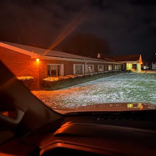 A view of a building at night, illuminated by warm lights, with a snowy landscape in the foreground.