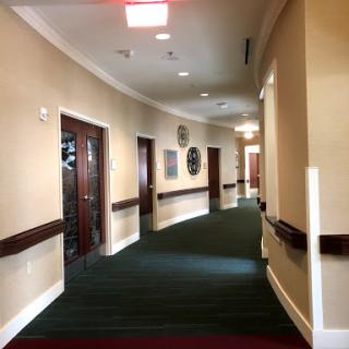 A view of a well-lit hallway with carpeted floors and doors along the sides.