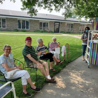 A group of elderly individuals enjoying a sunny day outside, sitting on benches and engaging in conversation.