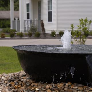 A fountain in a landscaped garden area near a house.
