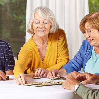 A group of seniors playing cards at a table indoors, smiling and enjoying their time.