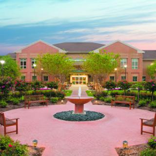 A serene garden area featuring a fountain and benches, surrounded by lush greenery and an inviting building.