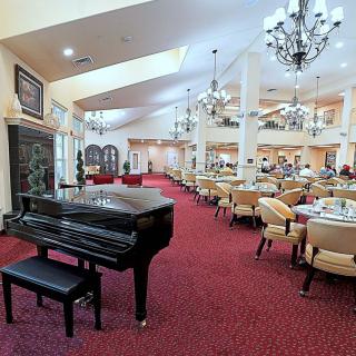 A spacious and elegant dining area features a grand piano, plush chairs, and ornate chandeliers.