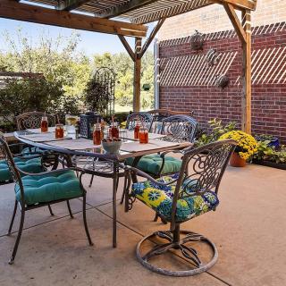 A cozy outdoor patio with a table and chairs under a pergola, surrounded by potted plants.