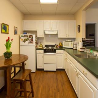 A cozy kitchen with white cabinets, featuring modern appliances and a small dining area with flowers on the table.
