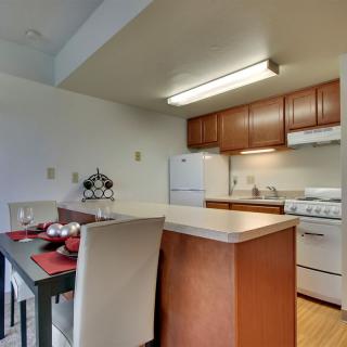 A modern kitchen and dining area in an apartment with wooden cabinets, a stove, and refrigerator.