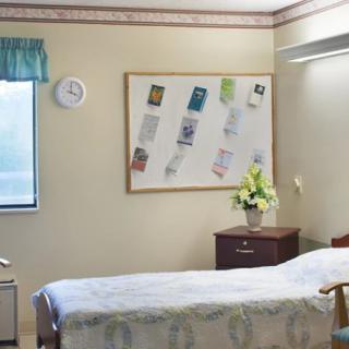 A neat and tidy hospital room with a single bed, wooden furniture, and a bulletin board on the wall.