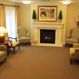 A cozy living room with a fireplace, featuring armchairs and traditional decor.
