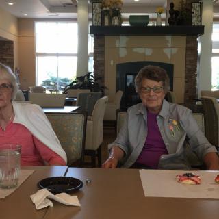Two seniors seated at a table, enjoying a meal indoors.