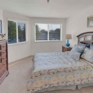 A cozy bedroom featuring a bed with patterned bedding, a wooden dresser, and large windows allowing natural light.