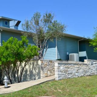 A residential house with blue siding and a stone wall, surrounded by trees on a sunny day.
