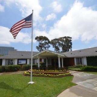 An American flag waves in front of a building surrounded by a landscaped garden on a partially cloudy day.