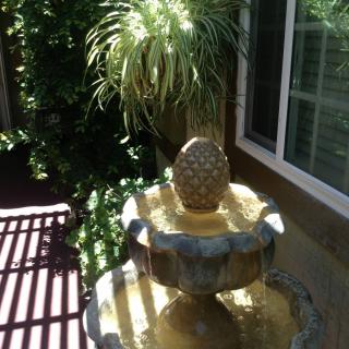 A garden fountain adorned with a pineapple ornament, surrounded by lush greenery and bathed in sunlight.