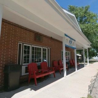 A brick building with a porch featuring red chairs and an awning on a sunny day.