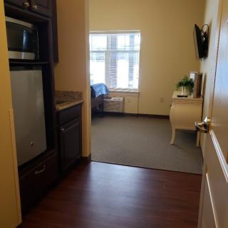 A small room with a kitchenette and a bed, featuring hardwood floors and a window.