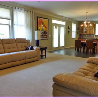 A spacious living room with beige sofas and an adjacent dining area, featuring large windows and modern decor.