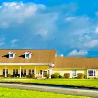 A charming yellow house under a vibrant blue sky with fluffy clouds, surrounded by a well-kept green lawn.