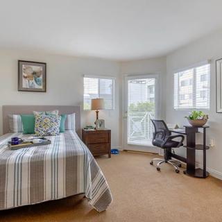 A cozy bedroom with a neatly made bed, a small desk and chair beside a window, and tasteful decor.