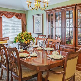 A traditional dining room with a wooden table set for a meal, surrounded by matching chairs and accented by a chandelier overhead.