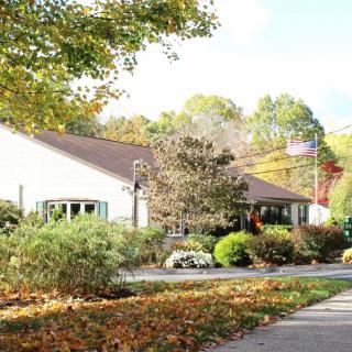 A peaceful building surrounded by autumn trees and foliage, with a sidewalk in the foreground.