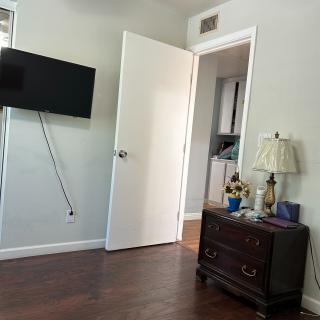 A cozy bedroom with an open door, wall-mounted television, and a dresser with a lamp.