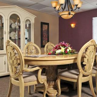 A classic dining room with an ornate round table and matching chairs, accompanied by a china cabinet and elegant chandelier.