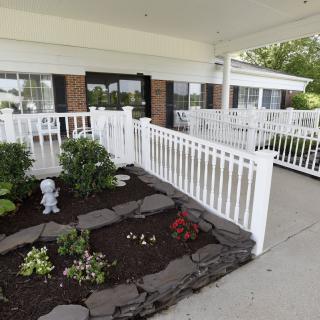A garden area with flowers and a small statue, bordered by a white railing on a porch.