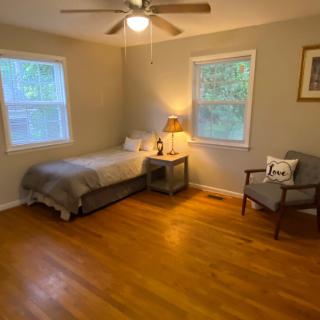 A minimalist bedroom with a single bed, wooden flooring, and a cozy chair.