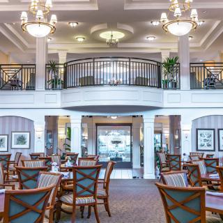 A spacious and elegant dining room with chandeliers, tables, and a balcony.