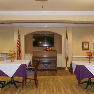 A cozy dining area with tables and chairs, decorated with flowers and flags, featuring a television on the wall.
