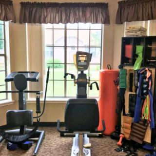 A cozy home gym with various exercise equipment, including an elliptical machine and yoga accessories, well-lit by natural light from the windows.