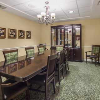 A well-furnished dining or conference room featuring a large wooden table surrounded by chairs, with artwork on the walls and a chandelier overhead.