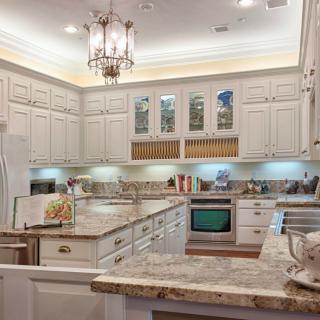 A well-designed kitchen featuring elegant cabinets, marble countertops, and a decorative chandelier.