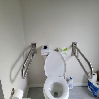 An accessible bathroom featuring a toilet with support handrails and hygiene products.
