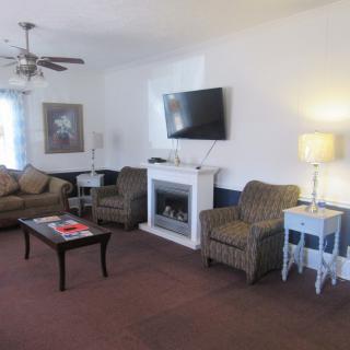A cozy living room with a sofa and armchairs arranged around a fireplace, topped with a flat-screen TV. A coffee table and lamp complete the setup.