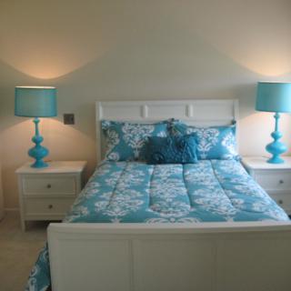A stylish bedroom featuring a bed with turquoise bedding and matching lamps.