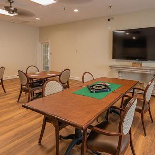 A cozy game room with multiple tables, chairs, and a large television.