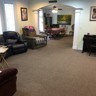 A cozy living room with recliners and a piano, leading into a dining area.