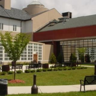 A modern building with large windows and a landscaped garden area featuring benches and young trees.