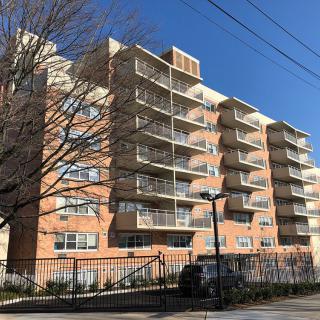 A multi-story apartment building with prominent balconies and a brick exterior on a clear day.