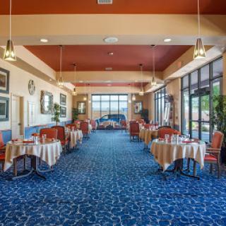 A spacious restaurant interior with neatly arranged tables and chairs, decorated with elegant lighting and large windows.