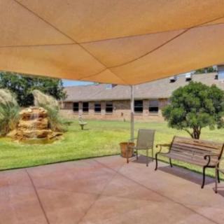 A cozy patio area with a shade sail, a bench, and a view of a garden fountain.
