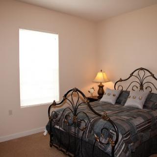 A cozy and well-lit bedroom featuring an iron bed with comfortable bedding and a bedside lamp.
